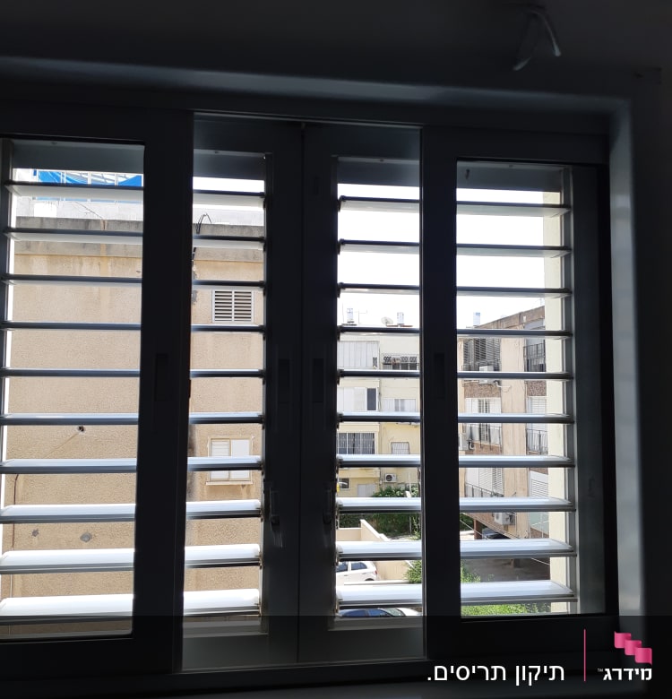 תריסים לבנים פתוחים עם נוף בניינים ברקע